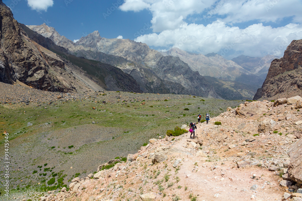 Group of Hikers on Orange Footpath Men and Women going with Hiking Gear sporty Clothing on bright Mountain Landscape background with blue sky and Valley View Behind