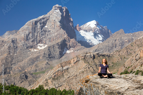 Young woman doing exercise Female Athlete Sitting in Yoga Zen Mediation Pose Mountain Panoramic Landscape Outdoor Orange Rocks Green Forest Clear Blue Sky High Summit with Snow Top on Background