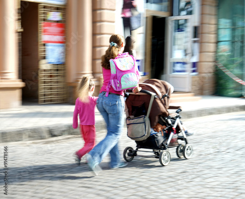 Fototapeta Naklejka Na Ścianę i Meble -  Young family with small child and a stroller walking down the st