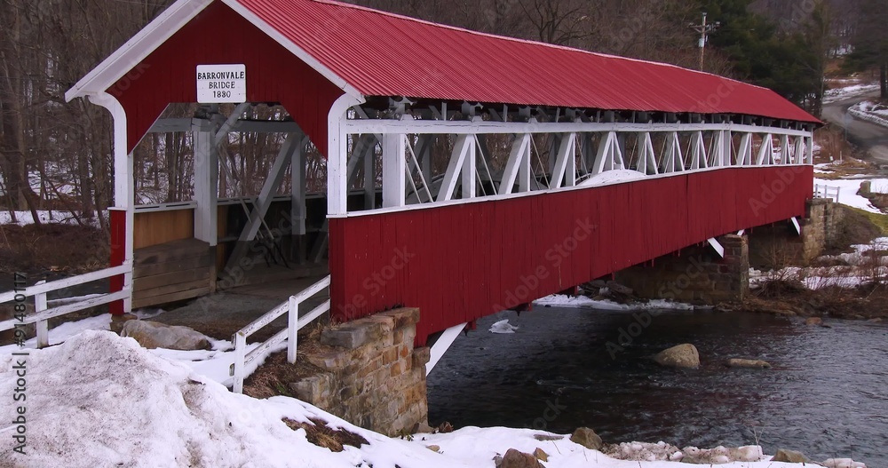 A pretty red covered bridge over a river in winter.