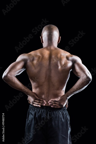 Rear view of muscular athlete stretching with hand on hip