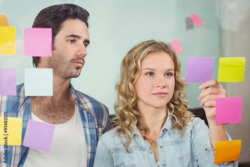 Man looking at woman sticking notes on glass Man looking at woman sticking notes on glass