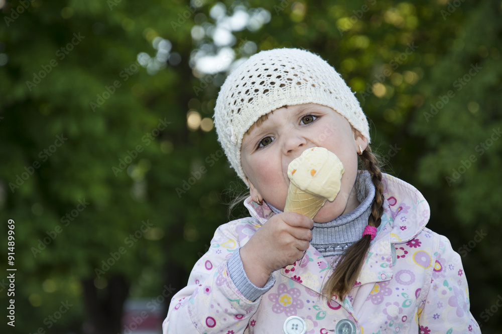 In the spring on the street a little girl eating ice cream. - obrazy, fototapety, plakaty 