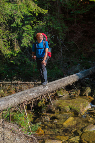 Hiker crosses mountain river by a makeshift bridge.