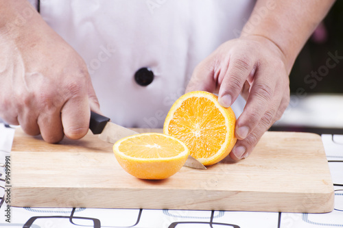 chef cutting orange on old wooden broad
