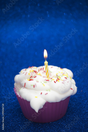 Cupcake with a lit candle over bright blue background