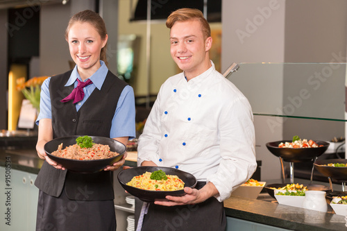 cook and waitress from catering service posing in front of buffet