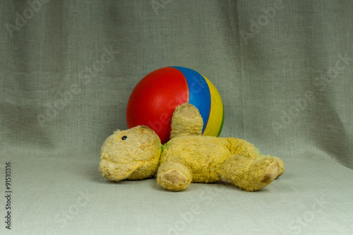 Old yellow teddy bear with a striped ball photo