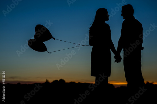 Silhouette of an in love couple with 2 heart balloons. 