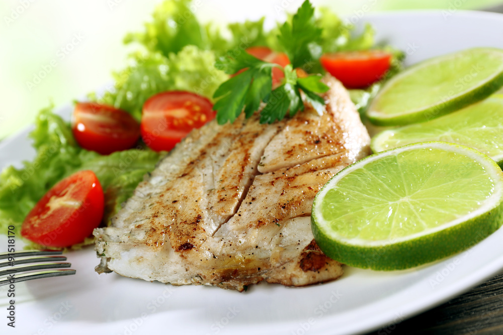 Dish of fish fillet with salad and lime on plate close up Dish of fish fillet with salad and lime on plate close up