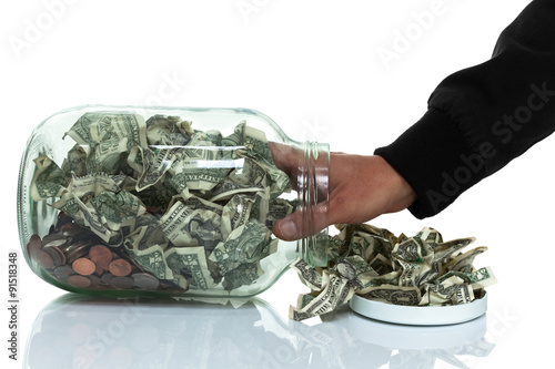 Glass jar full of money tipped over on its side spilling money w