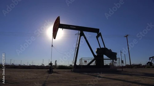 Establishing shot of an oil field with derricks pumping against the sun.