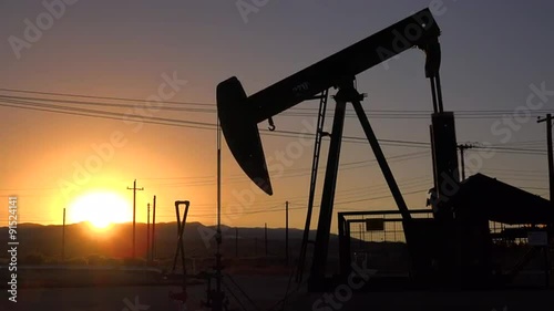 An oil derrick pumps against the sunset.