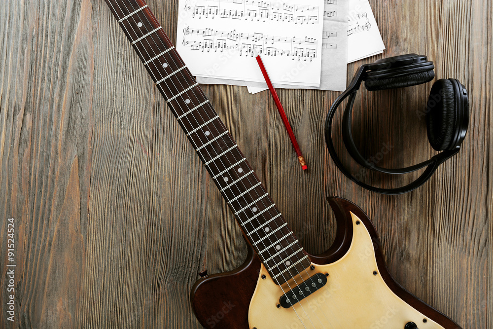 Fototapeta premium Electric guitar with headphones and music notes on wooden table close up