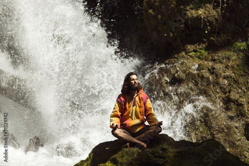 Young man meditating next to waterfall in the mountains