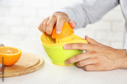 Young man using citrus-fruit squeezer, preparing orange juice