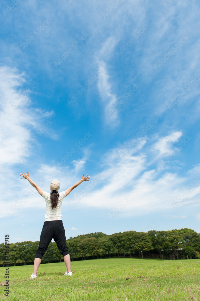 青空に向かって手を広げている女性の後ろ姿