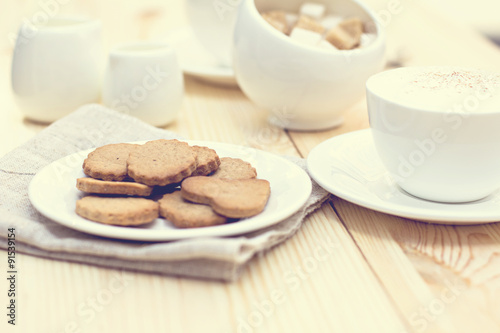 Ginger biscuits, cinnamon, a cup of hot coffee. Walnuts, hazelnuts on a wooden background. Tonned photo.