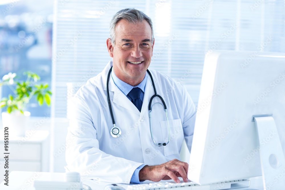 Smiling male doctor using computer in clinic Smiling male doctor using computer in clinic