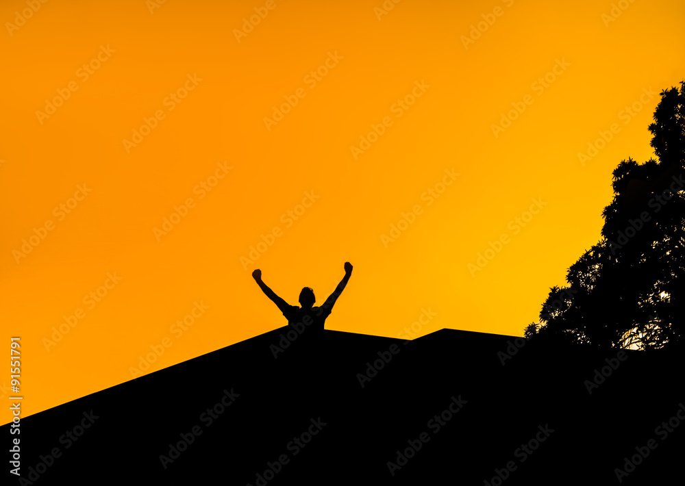 Silhouette of a man with hands raised in the sunset. Man on roof