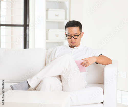 casual asian man reading in livingroom