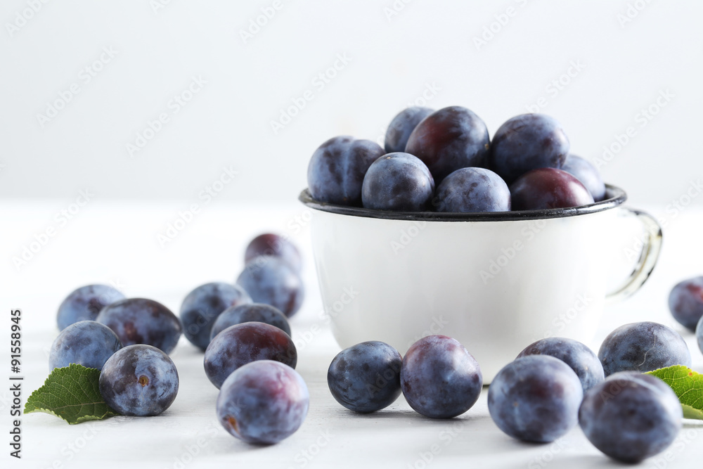 Fresh plums in cup on white wooden background Fresh plums in cup on white wooden background