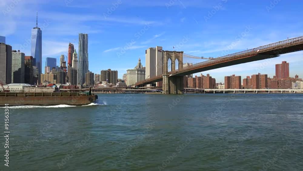 A barge and tugboat moves up New York's East River and crosses under the Brooklyn Bridge. A barge and tugboat moves up New York's East River and crosses under the Brooklyn Bridge.