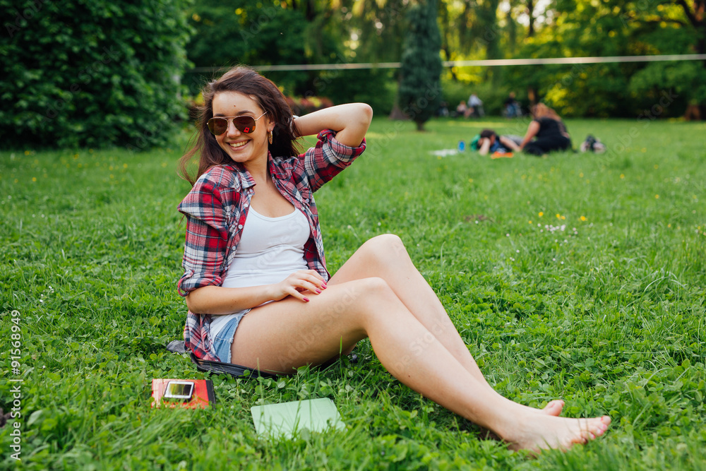 Fototapeta premium Brown hair girl spending free time, sitting on the grass in the park. 
