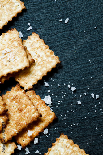 Crispy golden crackers with salt on dark stone background, top v