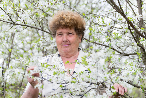 Pensive elderly woman in spring nature with cherry flowers