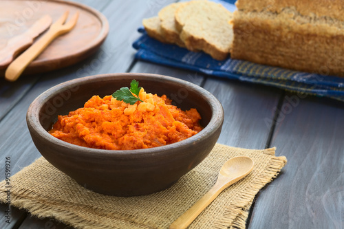 Carrot and red bell pepper spread in rustic bowl garnished with parsley leaf, wholegrain bread in the back, photographed with natural light (Selective Focus, Focus on the parsley leaf)