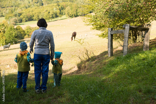 mother with two children watching horse and cheep on the pasture
