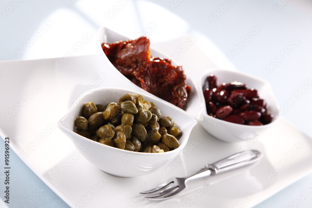 capers, tomatoes, beans in white bowls on a white background capers, tomatoes, beans in white bowls on a white background