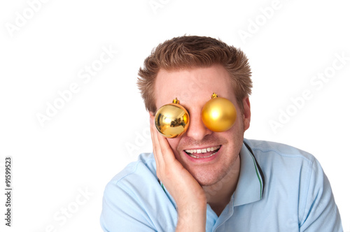 Junger lachender Mann mit Christbaumkugeln vor den Augen