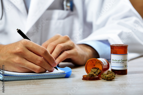 Doctor writing on prescription blank and bottle with medical cannabis on table close up