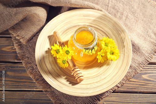 Honey with dipper and flowers on wooden tray