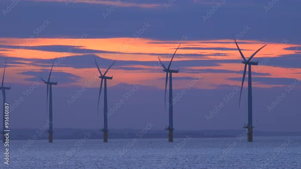 Windmills generate electricity along a coastline at sunset.