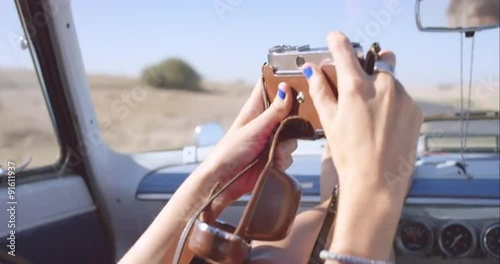 beautiful girl taking photos with vintage camera on road trip in convertible car