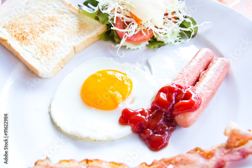 fried eggs with bacon, sausages and toasts on white plate