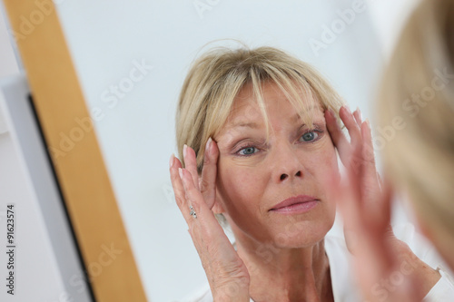 Senior woman looking at her skin in mirror