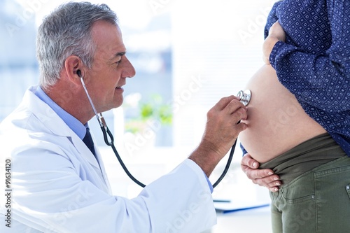 Canvas-taulu Male doctor examining pregnant woman in clinic