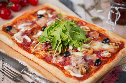 Homemade rectangular pizza on a rustic table with ingredients