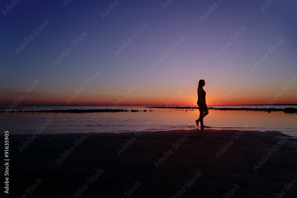teenage girl walking in water on beach in sunset