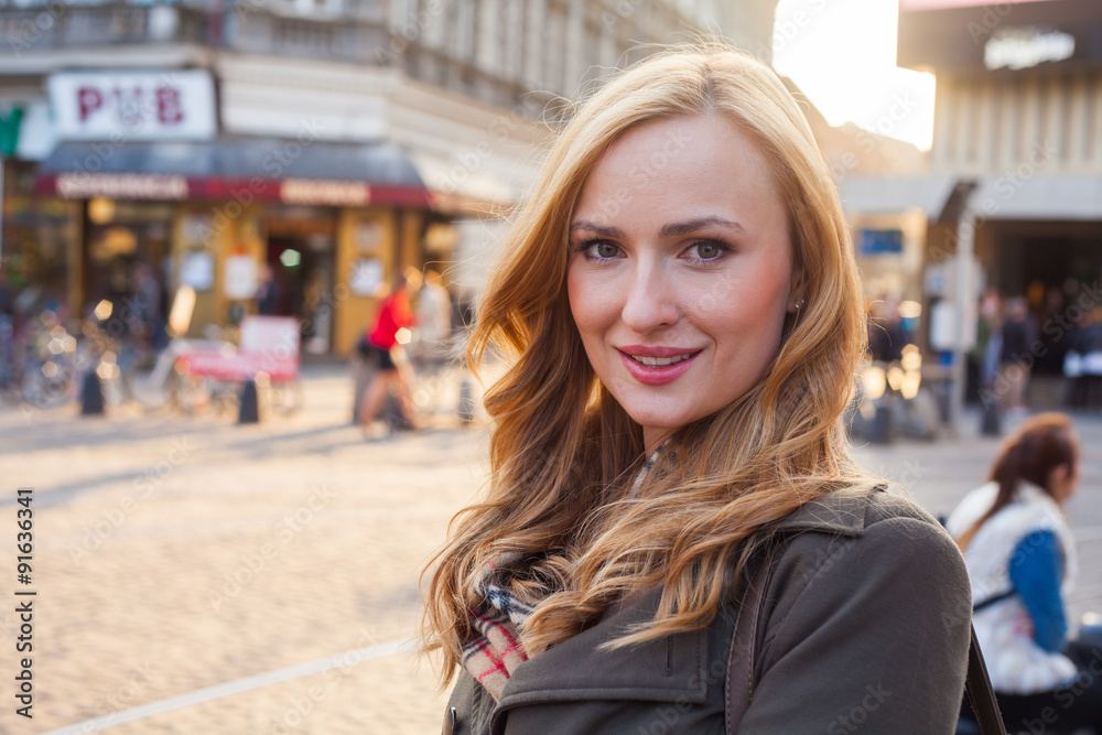 Beautiful blonde happy woman walking on the street in city. Outdoor photo.