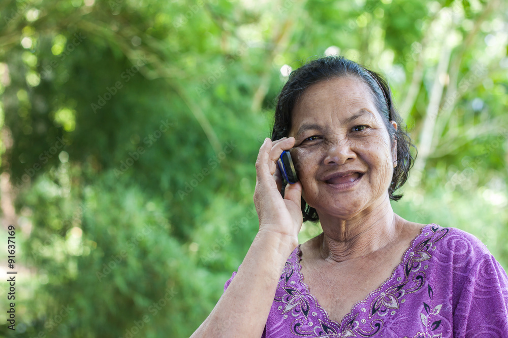 60 years old Thai woman smiling while talking on mobile phone 60 years old Thai woman smiling while talking on mobile phone