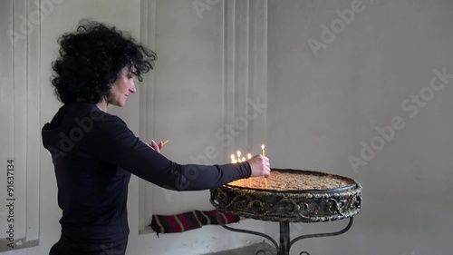 Religioous female lights candle and pray in church. UHD 4K steadycam stock footage photo