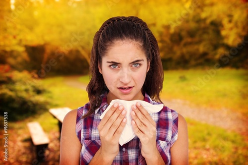 Composite image of portrait of sick woman sneezing in a tissue