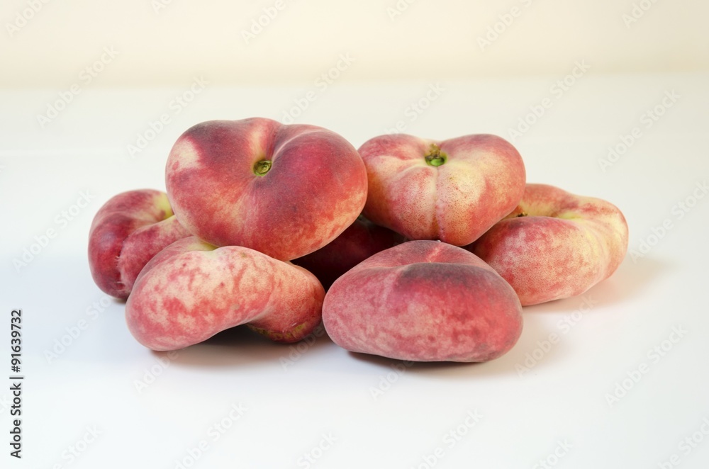 Six whole, medium-size, ripe, juicy saturn peaches shaped like a donut with a sunken middle, white skin with red blush isolated on background. An oddly doughnut like flat round peach yet tasty.