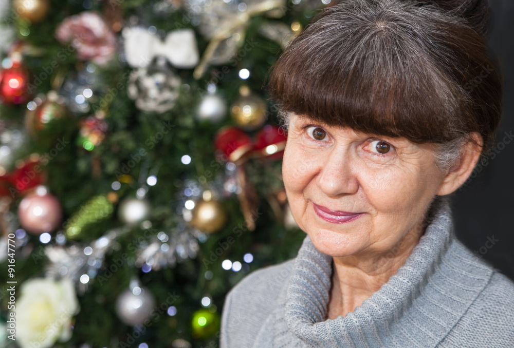 Mature age good looking woman against of Christmas tree. Christmas background
