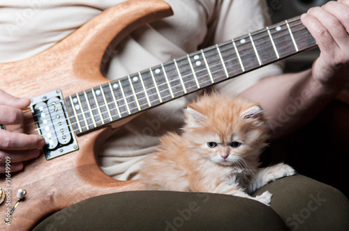 red kitten asleep in the arms of men playing the guitar